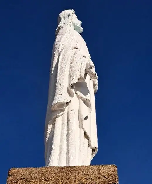 Estatua blanca del Corazón de Jesús sobre su pedestal, recortada contra el cielo